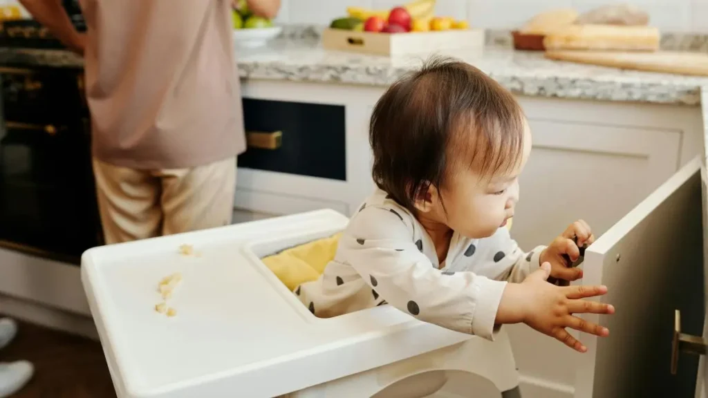 ベビーチェアに座り周囲に興味を示す赤ちゃんの様子。遊び食べ対策と親のメンタルを守るルール作りの解説画像。