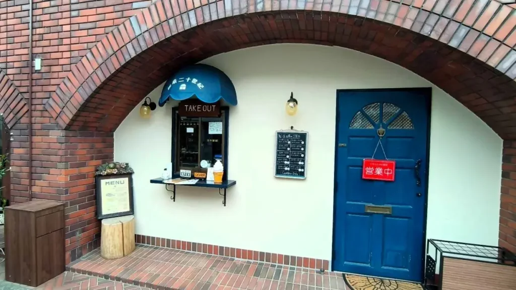 自由が丘に移転した「喫茶二十世紀」の外観。レンガ造りの壁に青いアーチの扉とテイクアウト窓口がある店構え。